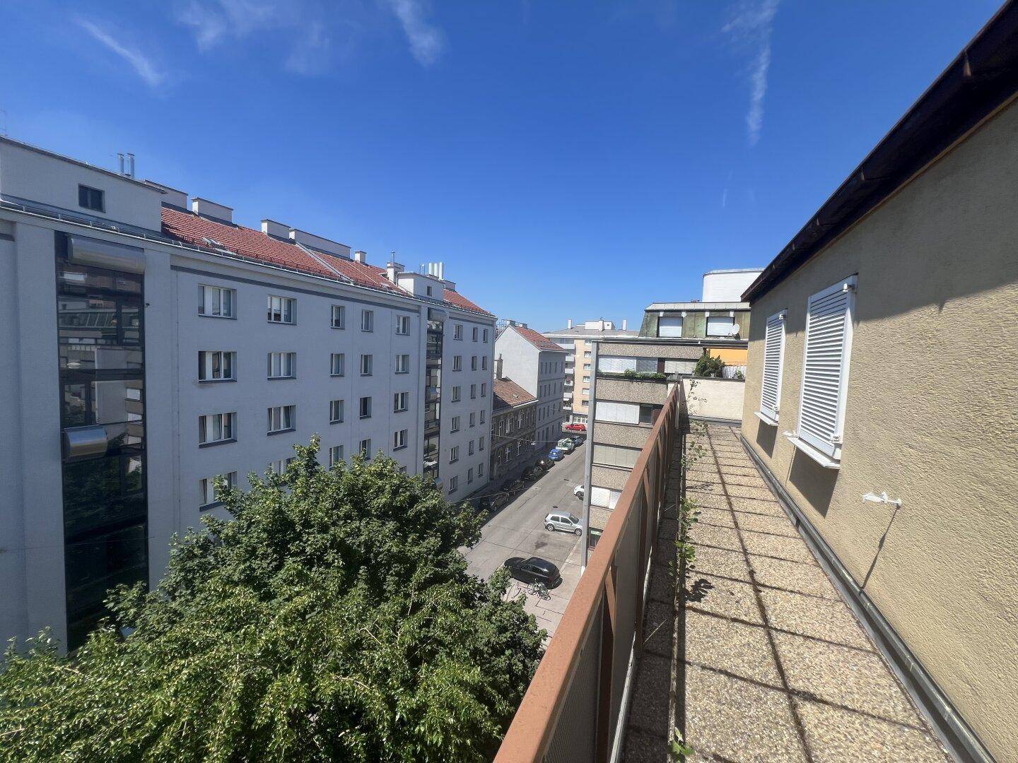 Langer Balkon mit Blick auf die Stadtstraße und umliegende Gebäude unter blauem Himmel.