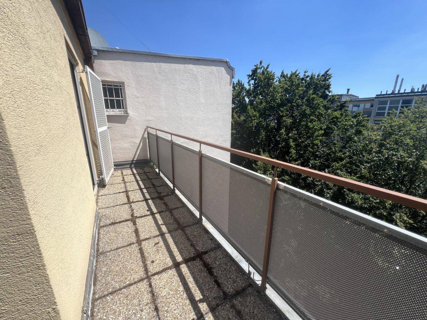 Schmaler Balkon mit Metallgeländer und Blick auf die umliegenden Gebäude und Bäume.