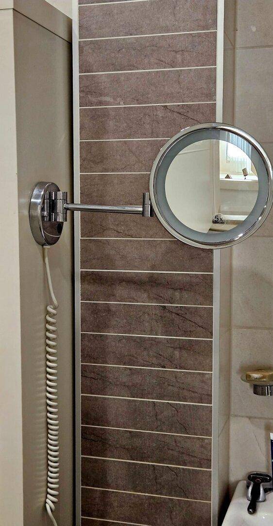 Detailaufnahme eines Badezimmerspiegels mit Vergrößerungsfunktion und Fliesenwand.