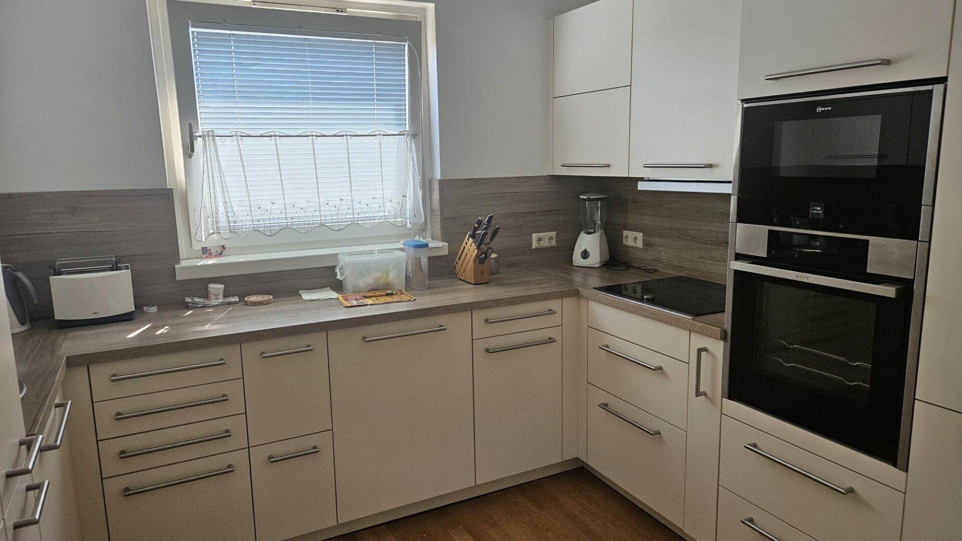 Moderne Einbauküche mit weißen Schränken, integrierten Geräten und Fenster.