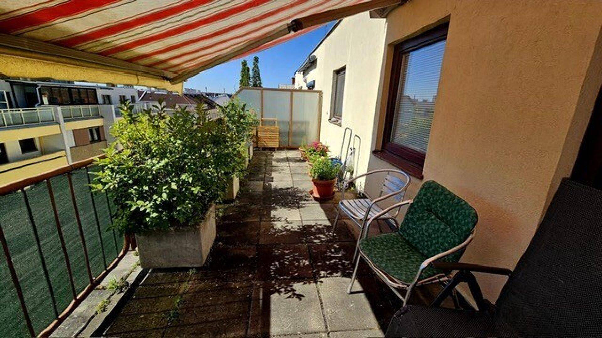 Geräumiger Balkon mit Fliesenboden, Pflanzen und bequemen Gartenmöbeln unter einer Markise.