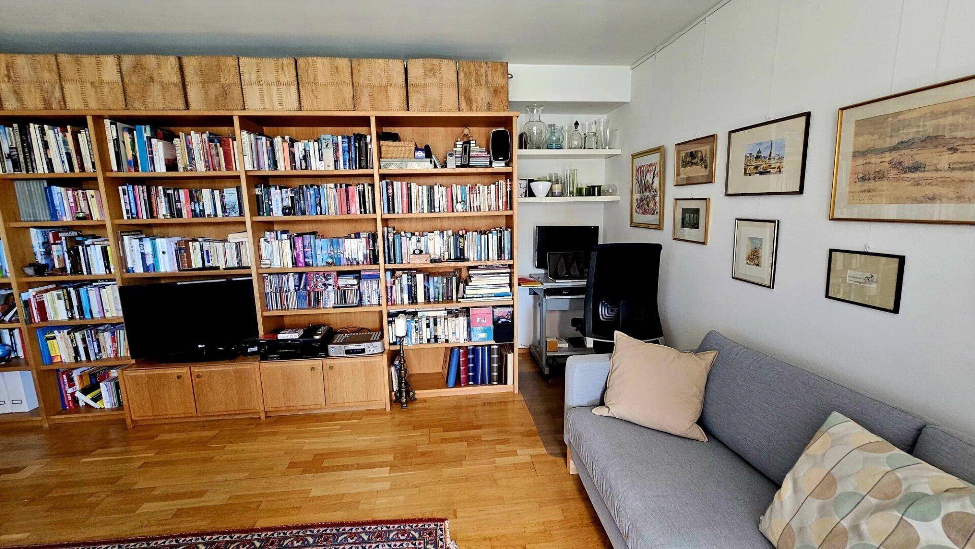 Geräumiges Wohnzimmer mit großer Bücherwand, bequemer Couch und Holzboden.