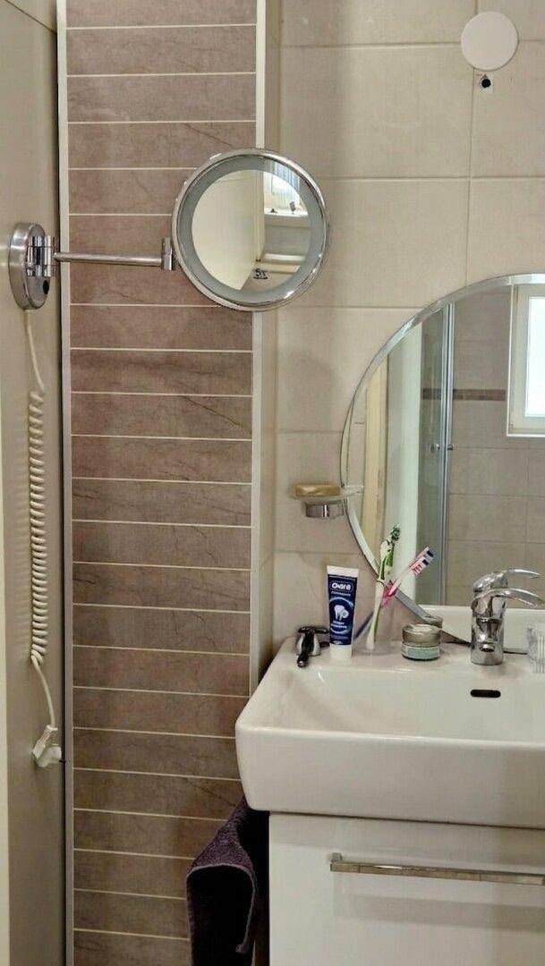 Modernes Badezimmer mit Waschbecken, Spiegel und praktischem Kosmetikspiegel.