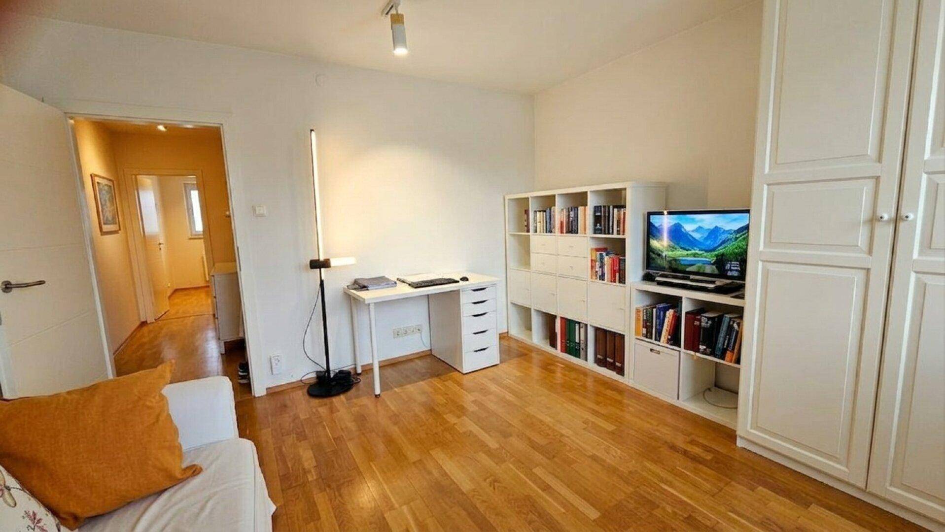 Helles Wohnzimmer mit Holzfußboden, Sofa, Schreibtisch und Bücherregal.