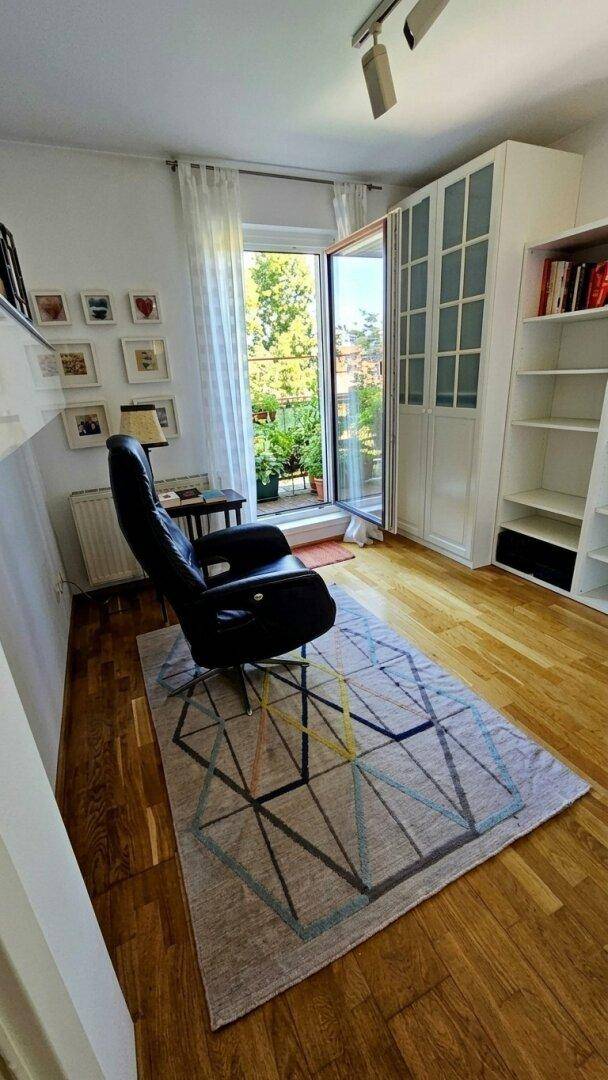 Helles Zimmer mit bequemem Sessel, weißen Schränken und Zugang zum Außenbereich.