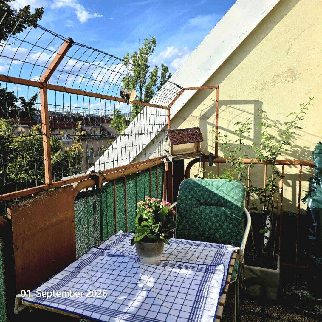 Kleiner, einladender Balkon mit Tisch und Stuhl, umgeben von Pflanzen und mit Blick ins Grüne.