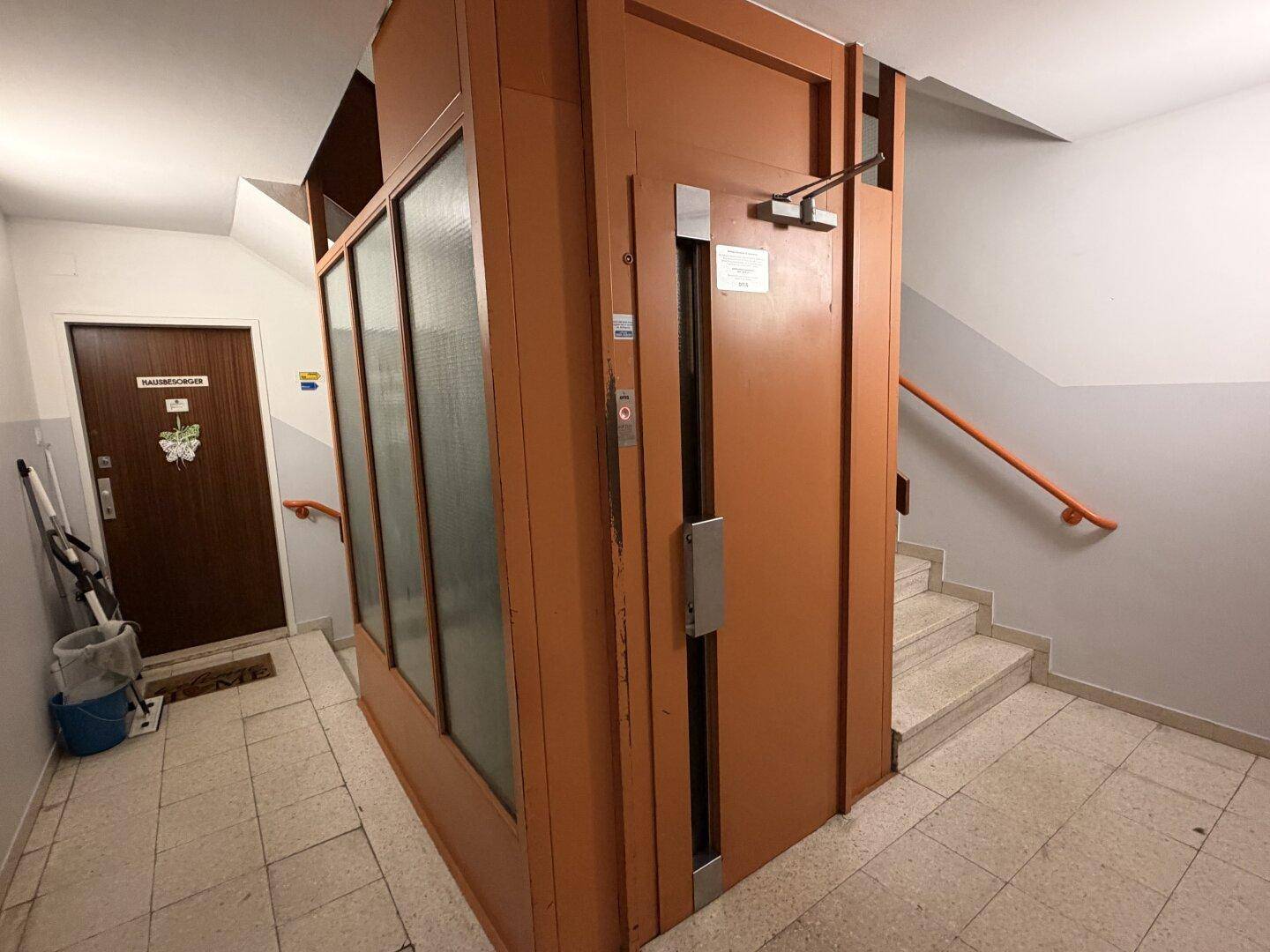 Gemeinschaftlicher Flur mit einem Aufzug und einer Treppe, die zu den oberen Etagen führt.