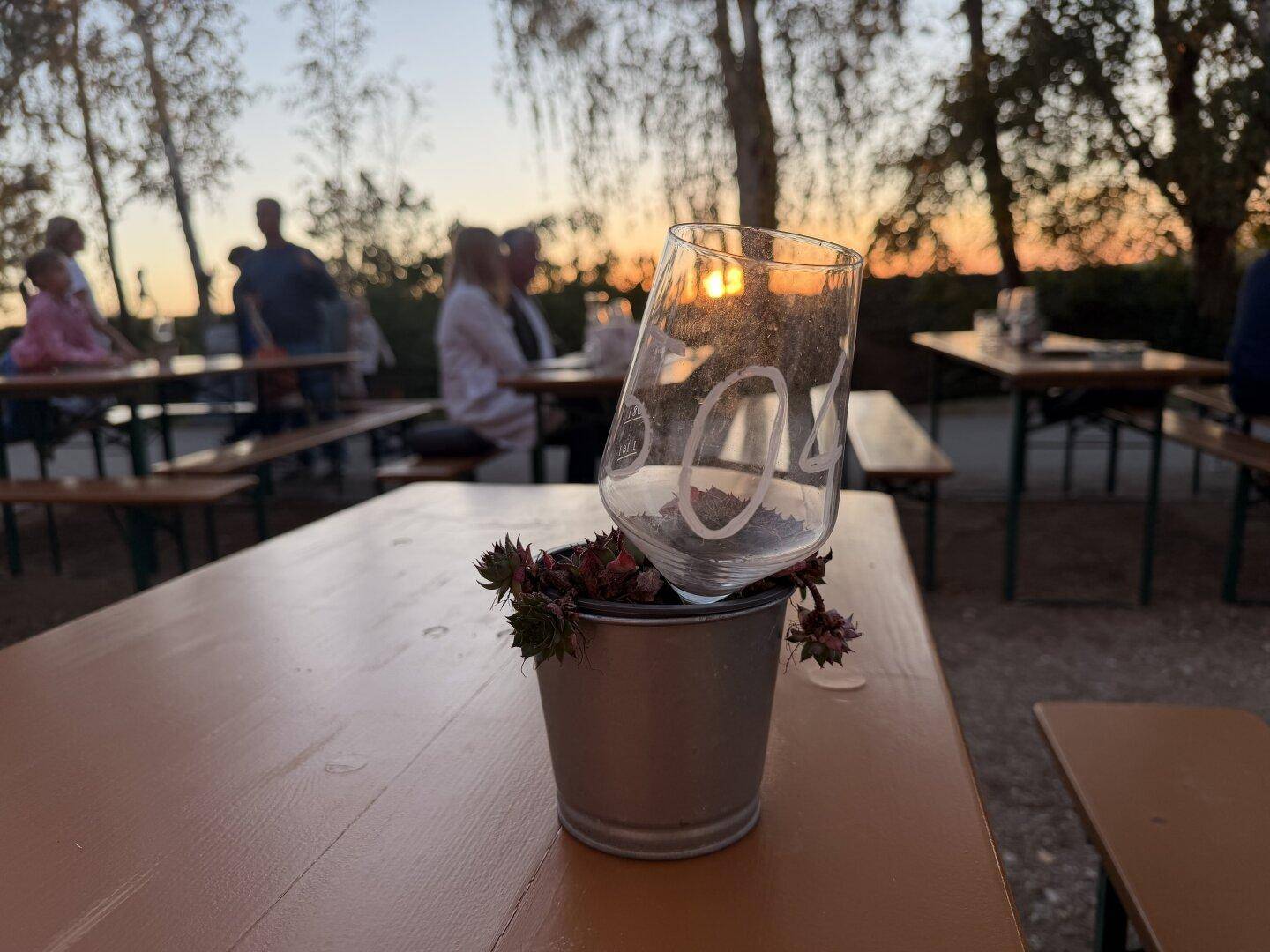 Nahaufnahme eines Weinglases auf einem Holztisch im Freien bei Sonnenuntergang.