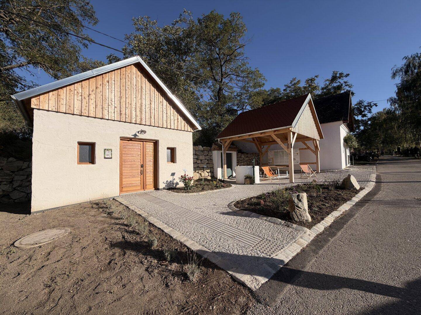 Zwei kleine Gebäude mit Holzelementen und einem gepflasterten Weg unter blauem Himmel.