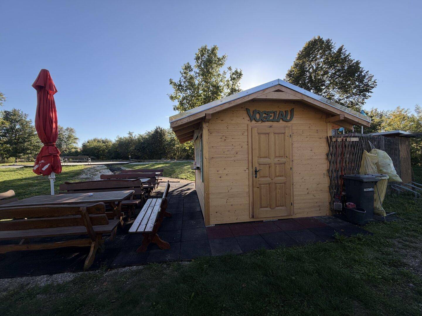 Kleines Holzhaus mit Sitzgelegenheiten im Freien und einem roten Sonnenschirm.