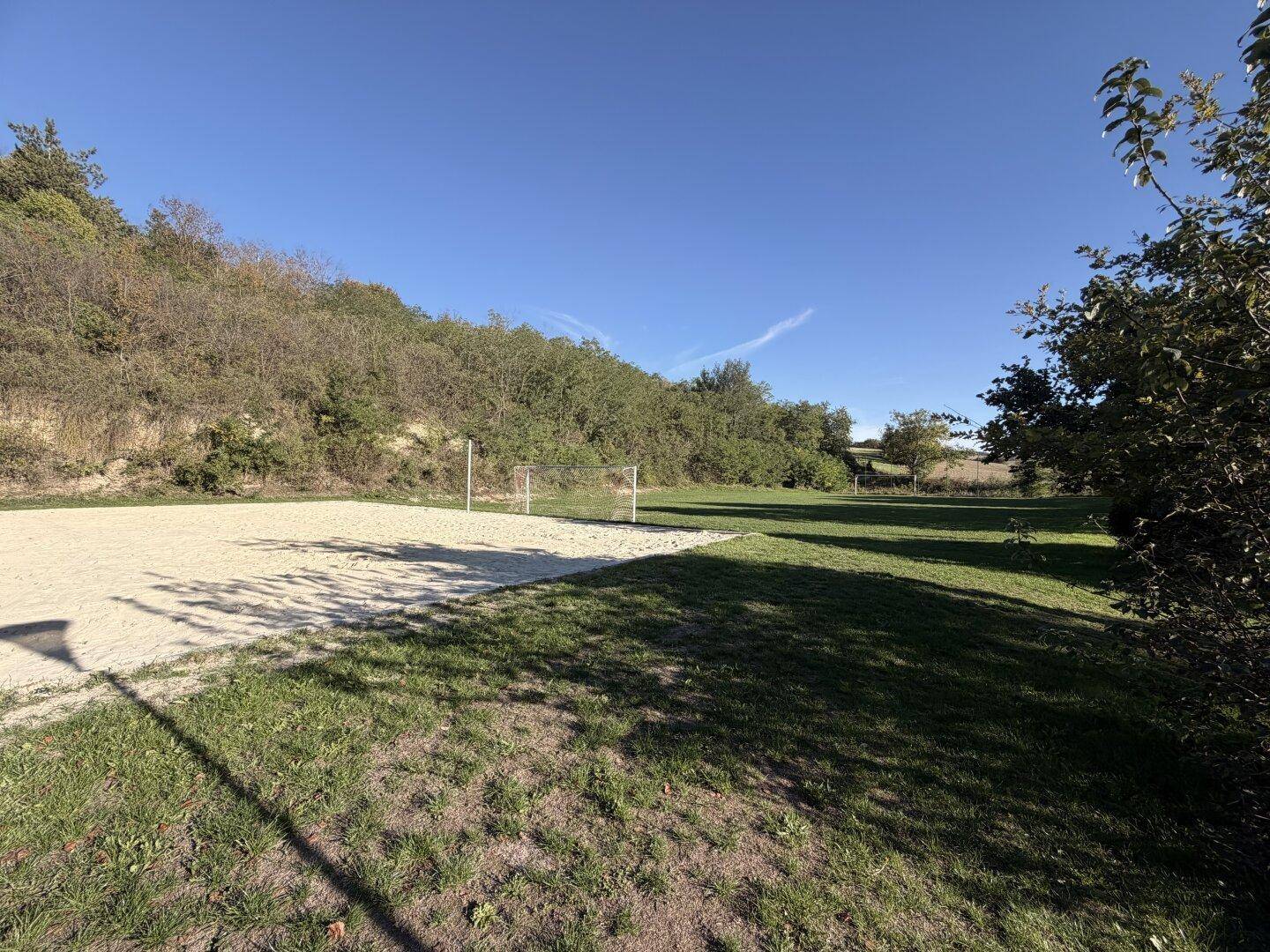 Ein Sportplatz mit Sand- und Rasenflächen, umgeben von bewaldeten Hügeln.