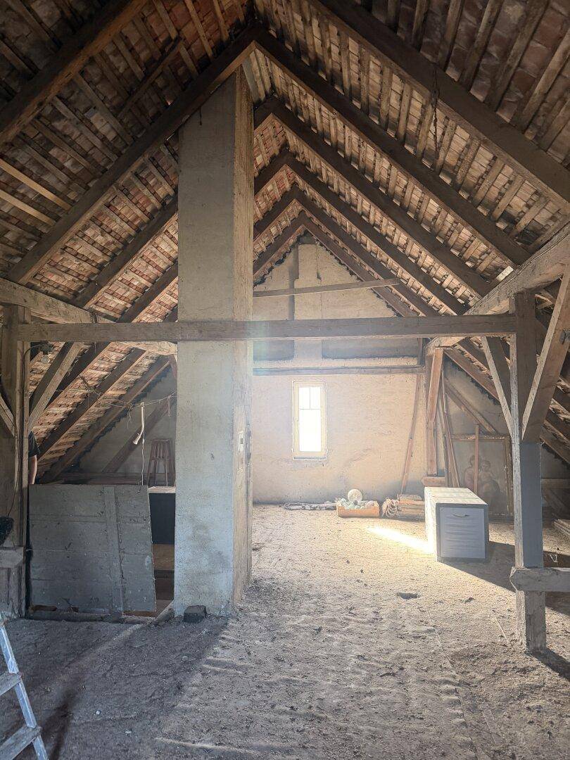 Geräumiger Dachboden mit sichtbaren Holzbalken und einem kleinen Fenster, bereit für den Ausbau.
