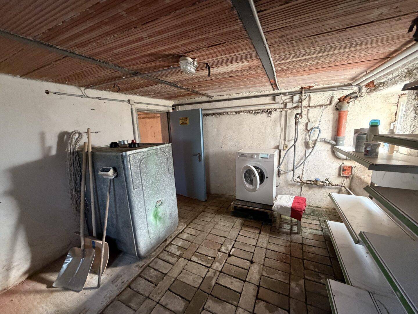 Kellerraum mit Waschmaschine, Heizöltank und sichtbaren Rohren, ideal als Abstellraum.