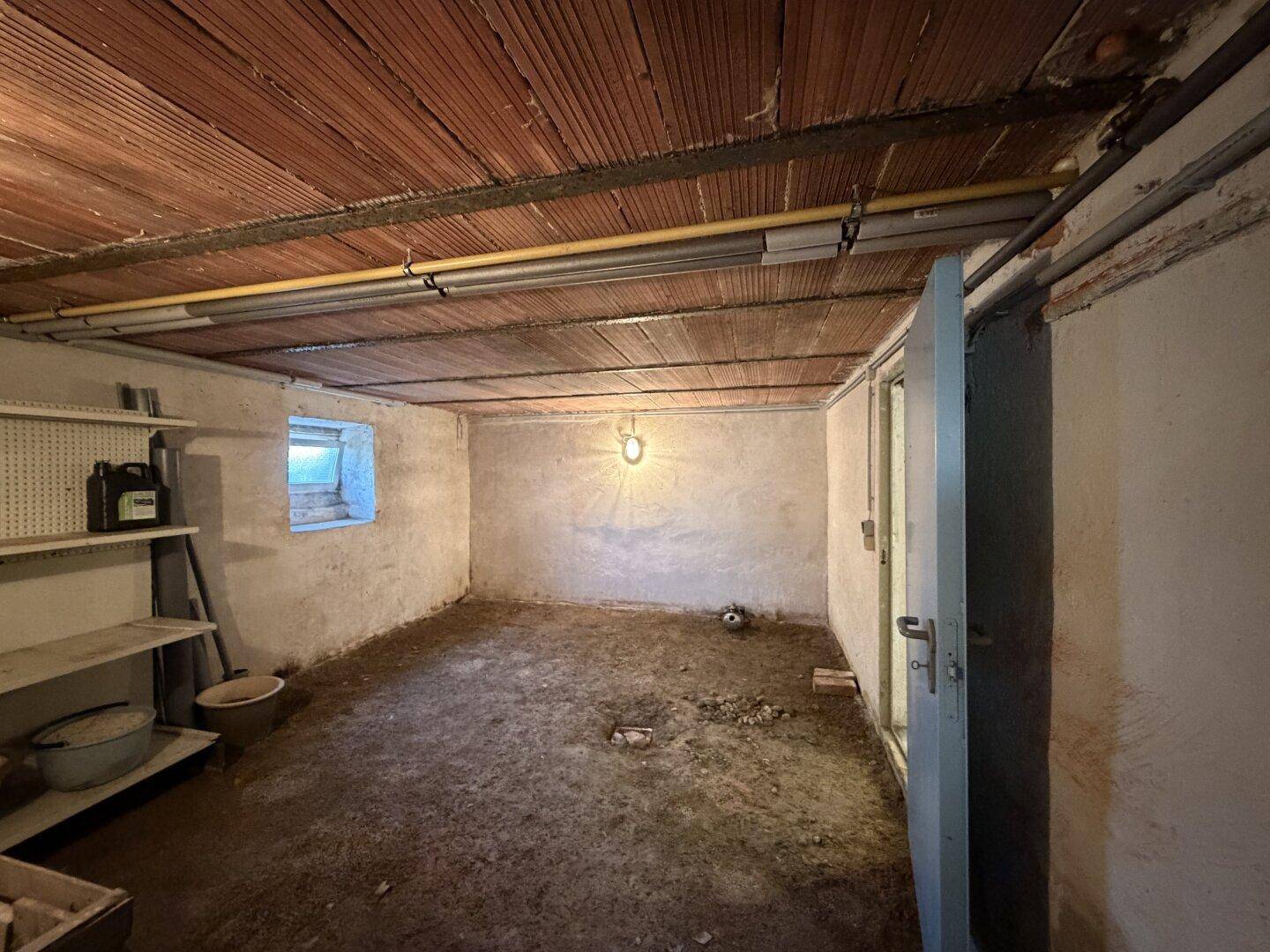 Leerer Kellerraum mit kleinem Fenster und einfacher Beleuchtung, ideal für Lagerzwecke.