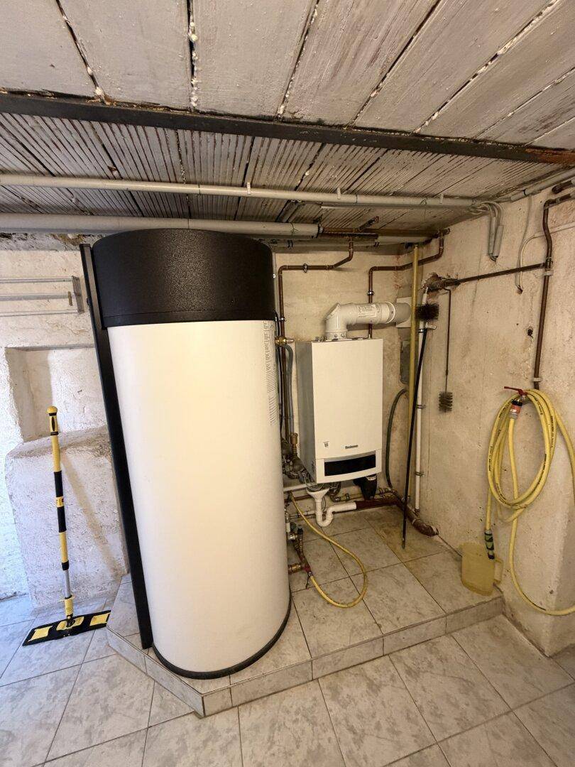 Heizungsraum mit modernem Boiler und Warmwasserspeicher auf gefliestem Boden.