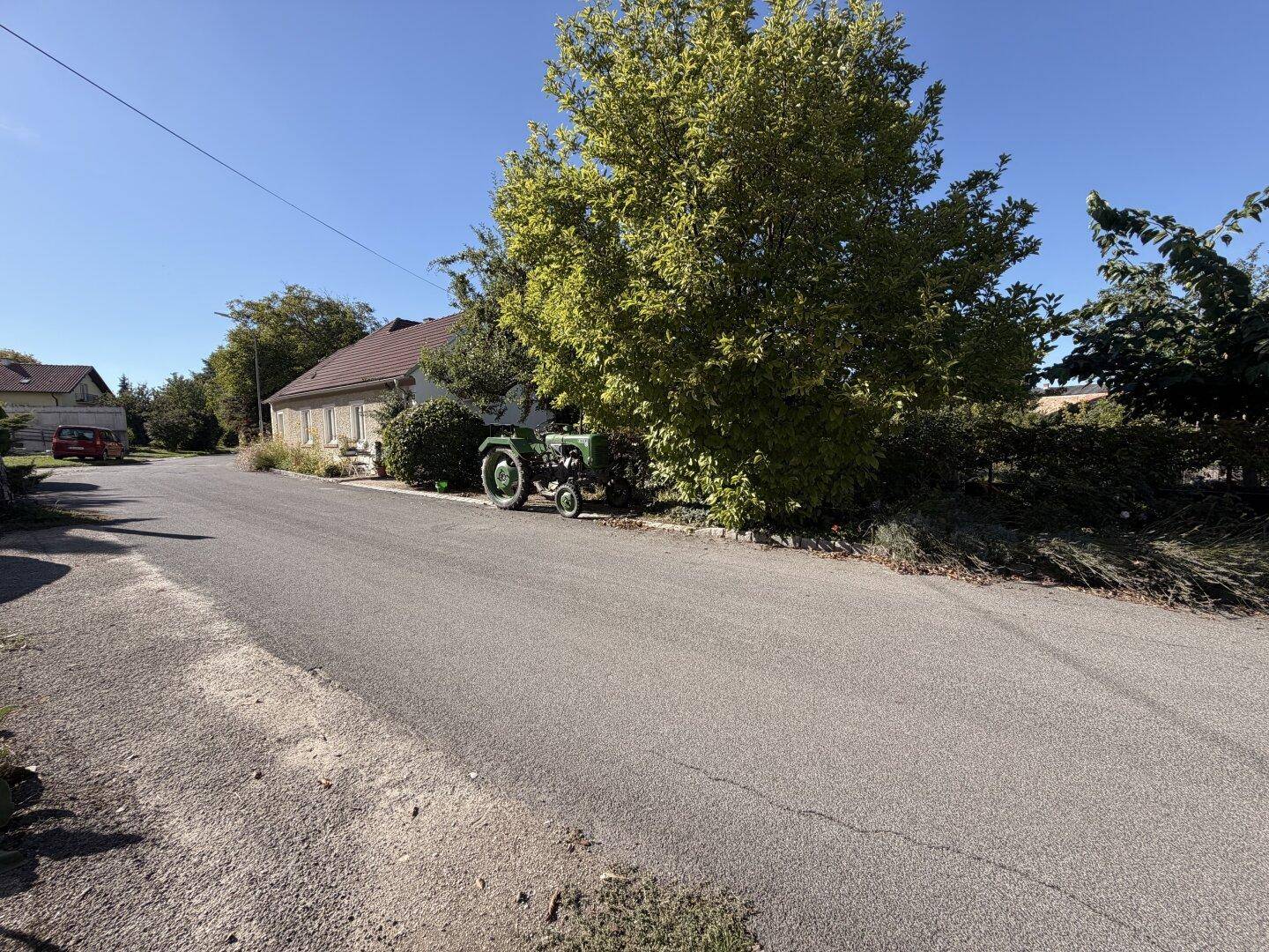 Ländliche Straße mit einem alten Traktor am Straßenrand und viel Grün.