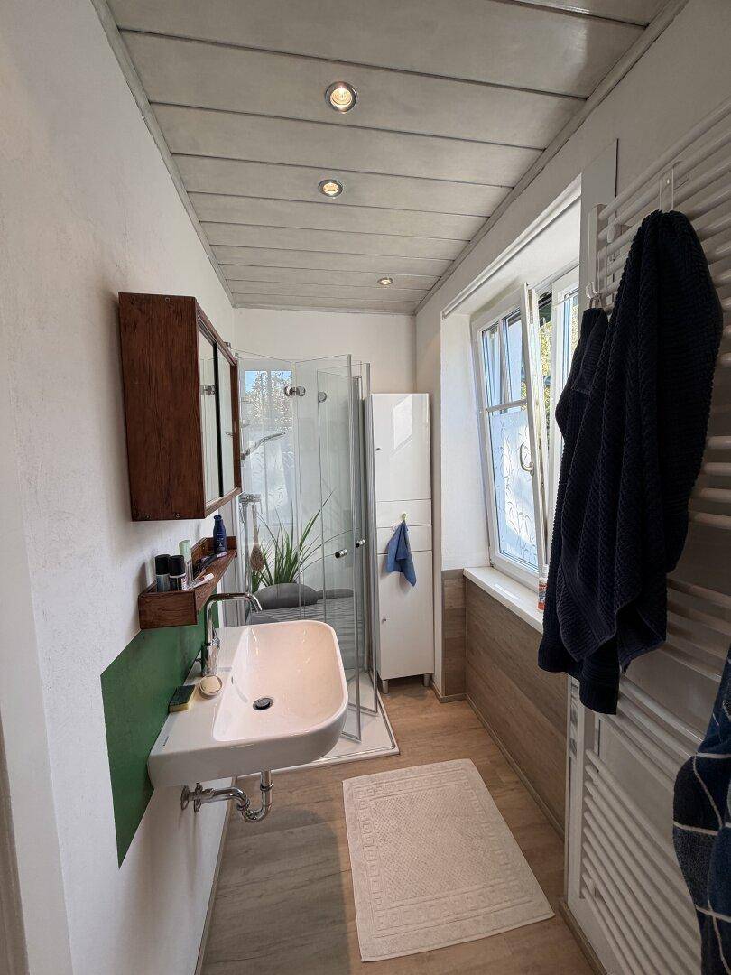 Modernes Badezimmer mit Duschkabine, Einzelwaschbecken, beheiztem Handtuchhalter und Fenster.