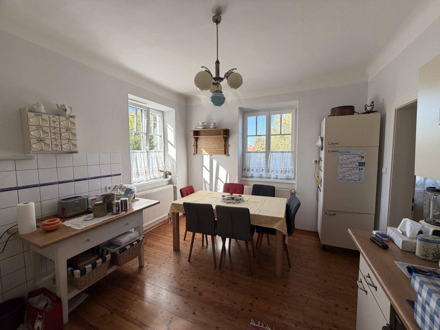 Geräumige Wohnküche mit Holzboden, Esstisch und traditionellen Fliesen an der Wand.