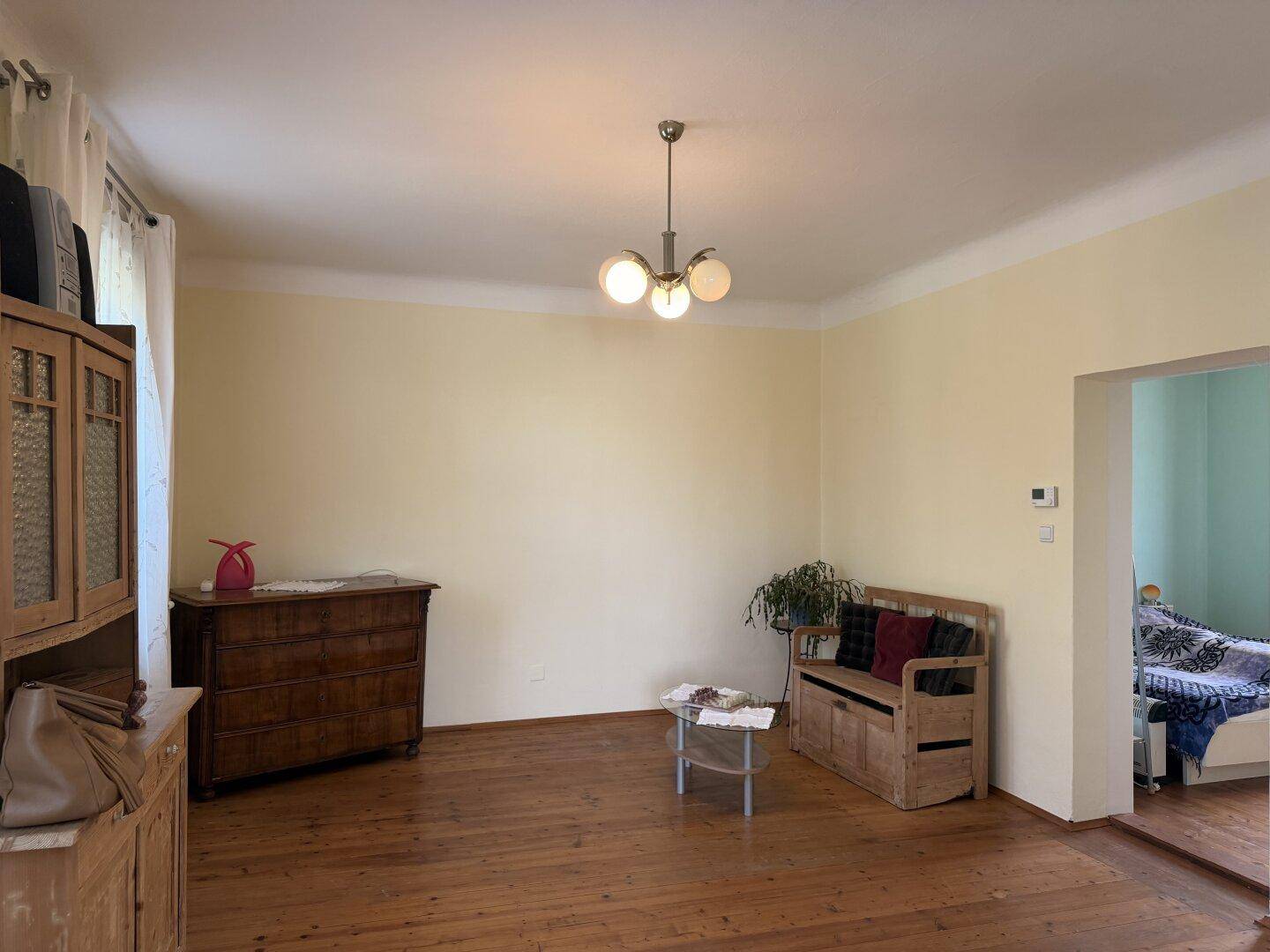 Wohnzimmer mit Holzboden und Zugang zu einem angrenzenden Raum, hell und funktional eingerichtet.