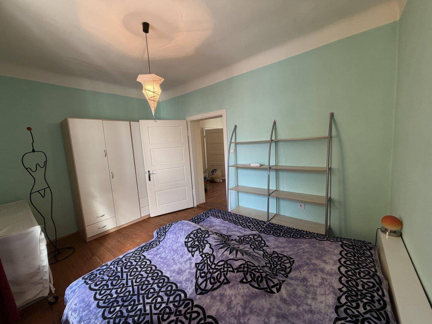 Schlafzimmer mit hellgrünen Wänden, Holzboden und praktischen weißen Kleiderschränken.
