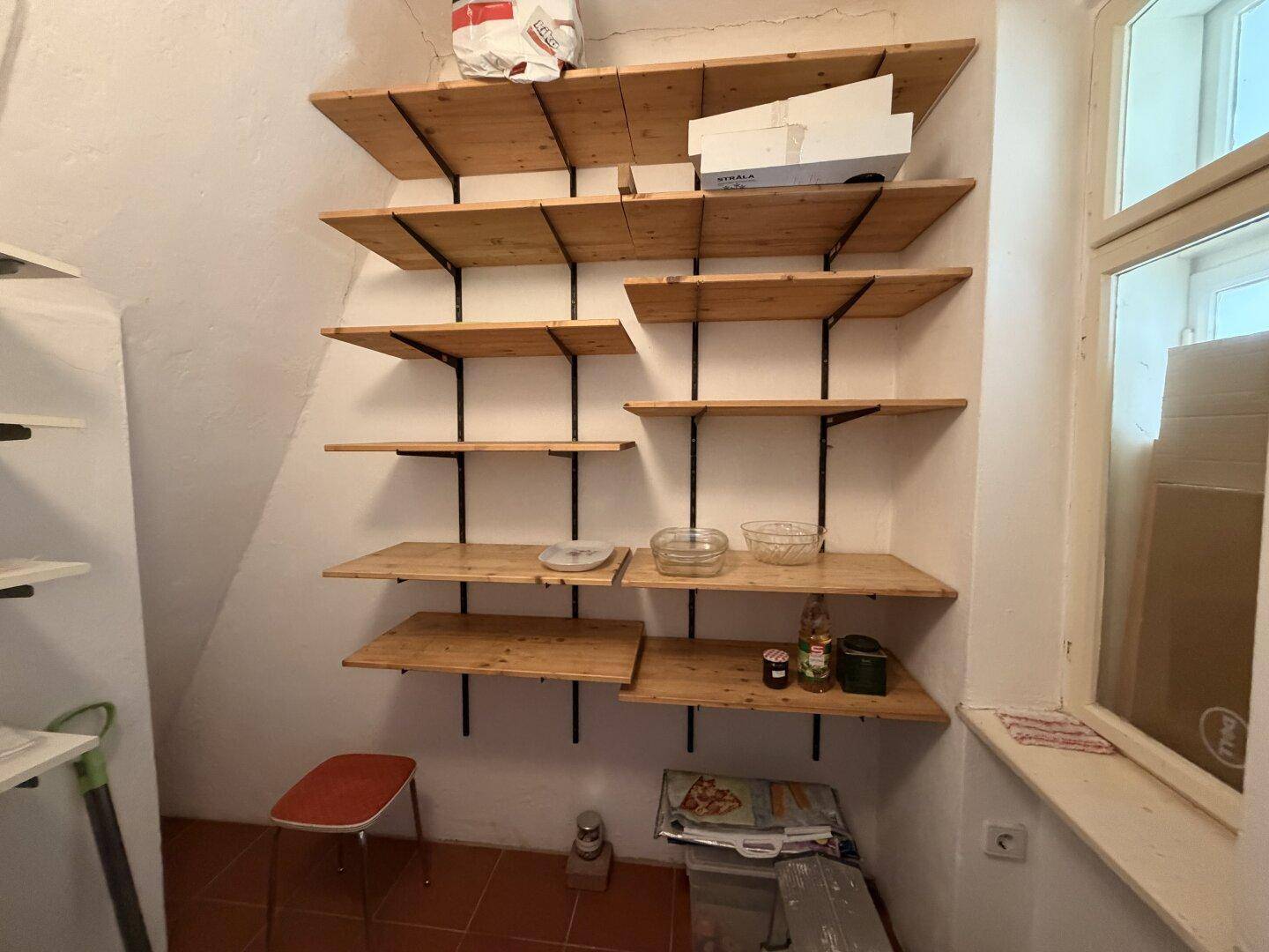 Praktischer Abstellraum mit vielen Holzregalen und einem kleinen Fenster, ideal für Vorräte.