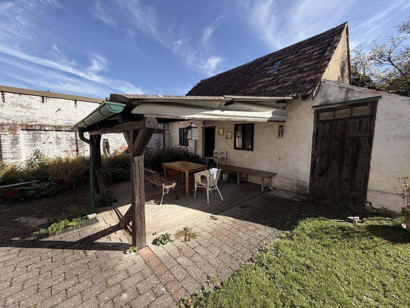 Gemütlicher überdachter Sitzbereich im Freien mit Holztisch und Stühlen, ideal für entspannte Stunden.