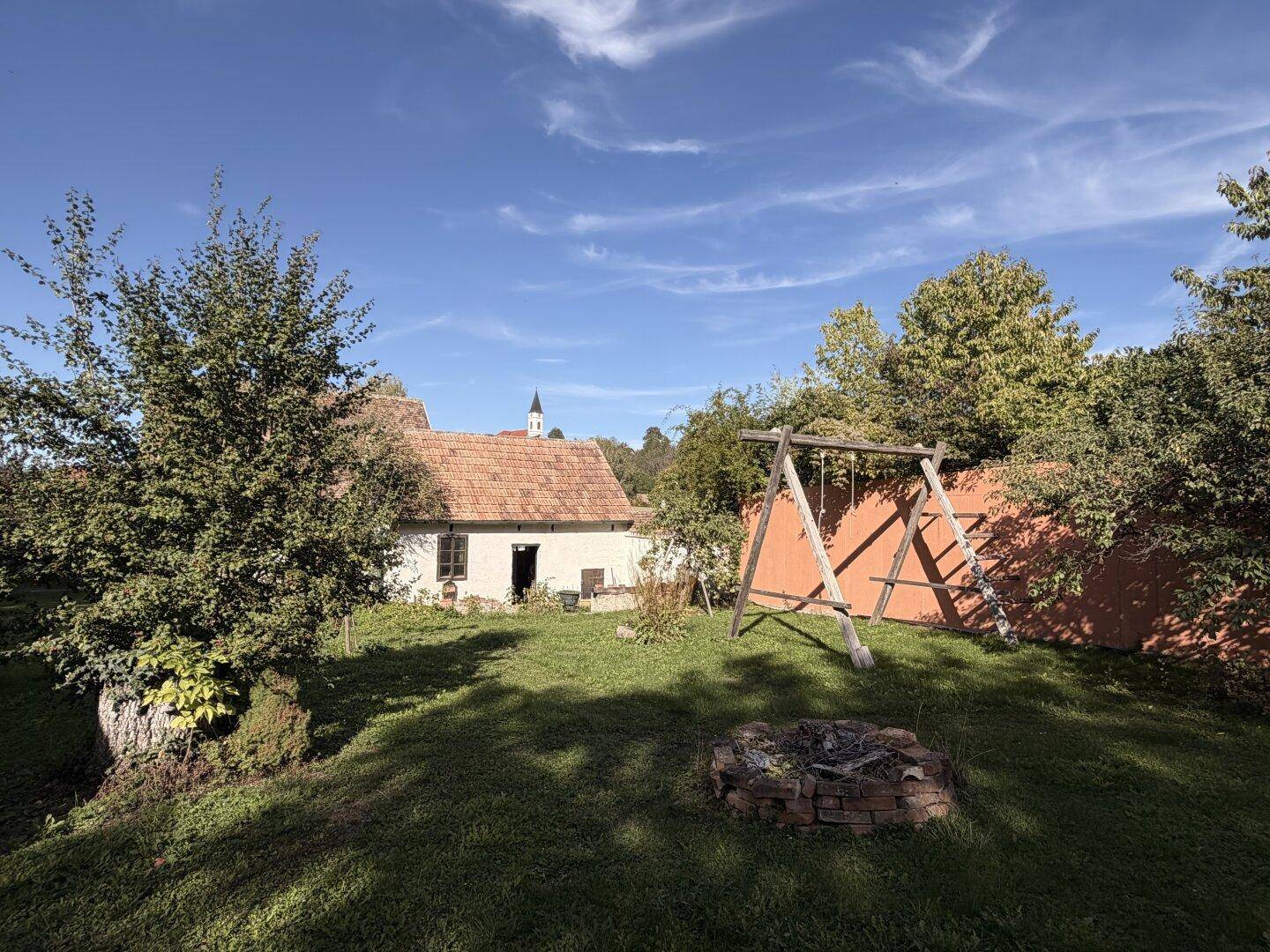 Großer Garten mit Schaukelgestell, Feuerstelle und Blick auf ein traditionelles Haus.