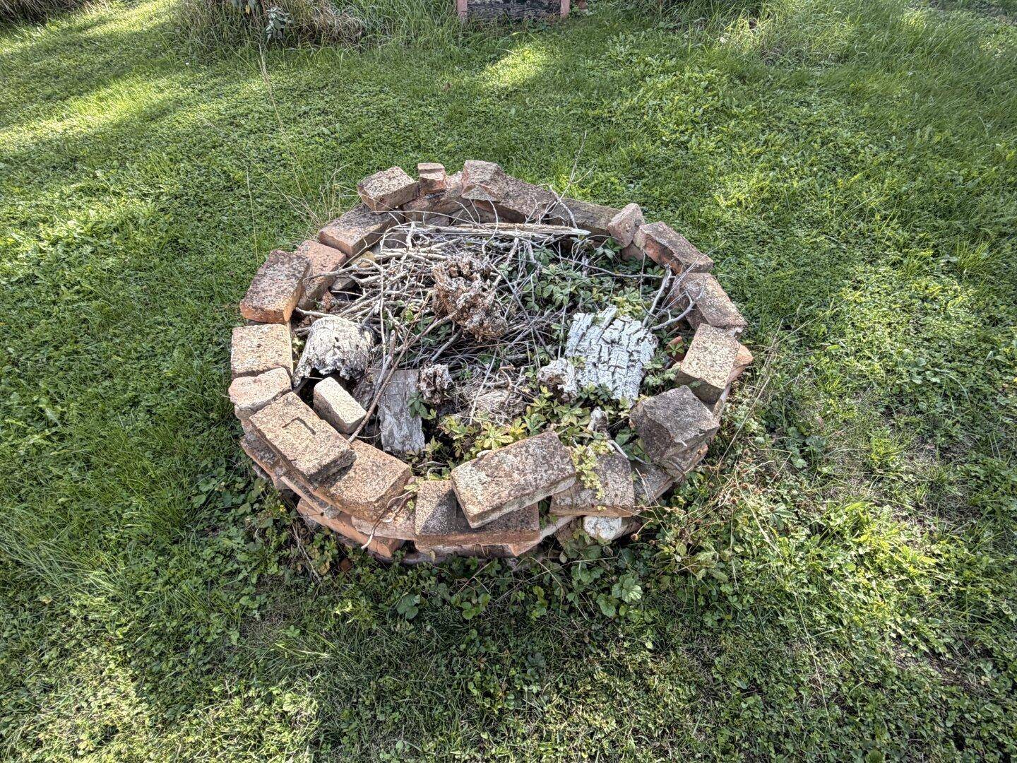 Runde Feuerstelle aus Ziegelsteinen im Gras, gefüllt mit Holz und Ästen.
