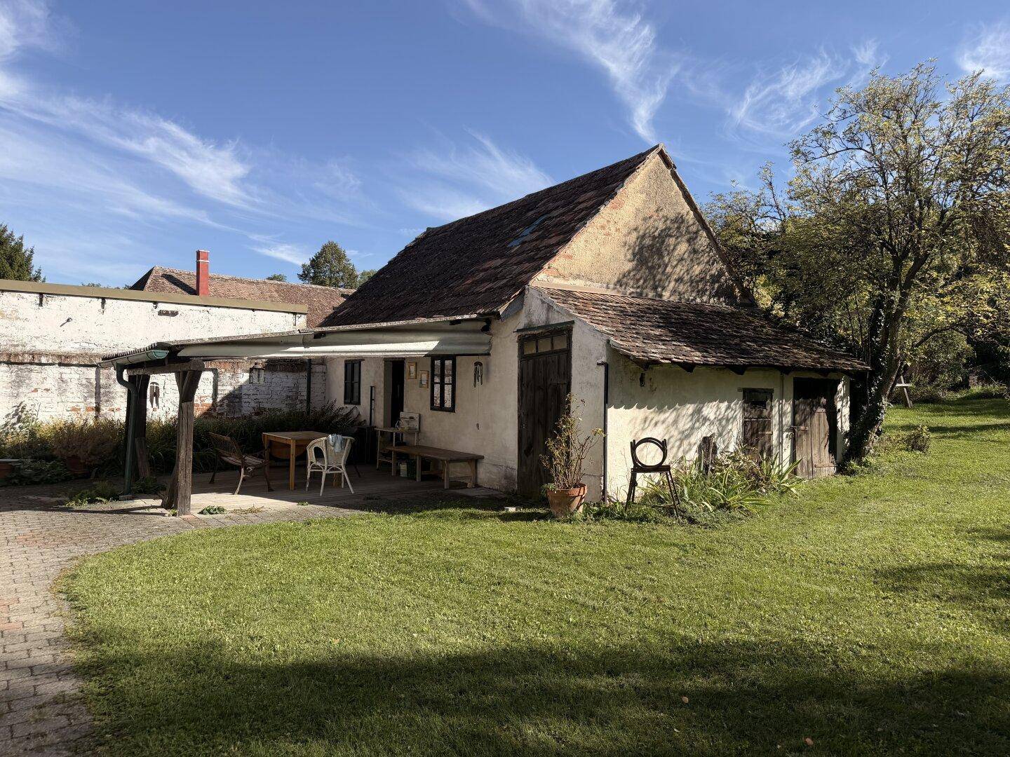 Rustikales Nebengebäude mit überdachter Terrasse und großem, sonnigen Gartenbereich.