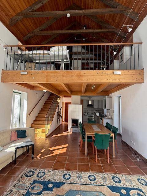 Offener Wohn- und Essbereich mit Galerie, Holzbalken und traditionellem Kachelofen.
