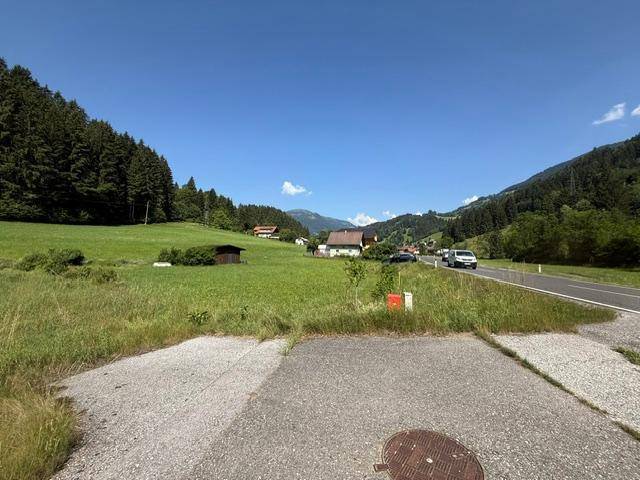Ländliche Landschaft mit grünen Wiesen, Wäldern und einer Straße mit Fahrzeugen.