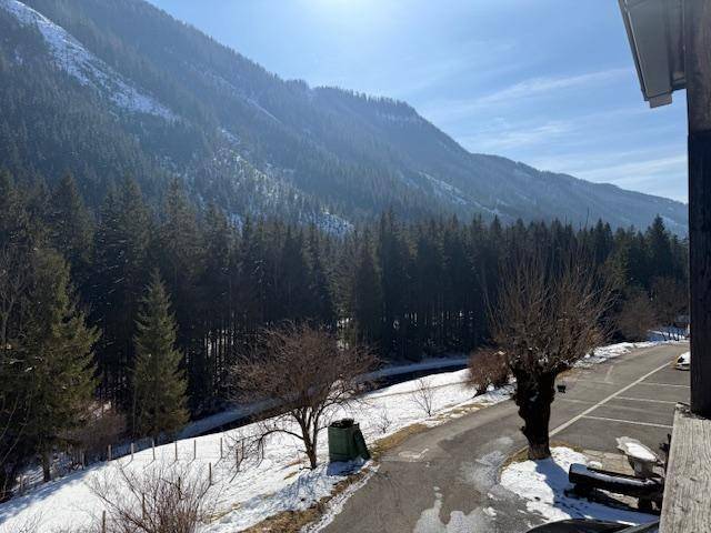 Weitläufiger Blick auf die Berglandschaft mit Wald, Straße und teilweise verschneiten Flächen.