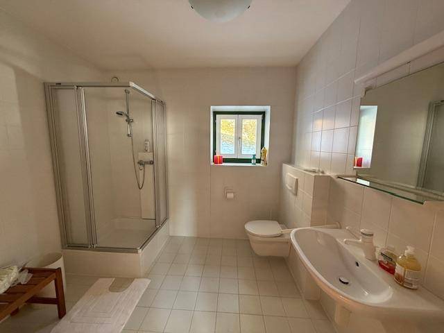 Modernes Badezimmer mit Duschkabine, WC und Waschbecken in hellen Fliesen.