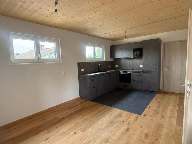 Moderne Einbauküche mit grauen Schränken, Holzboden und Holzdecke in einem hellen Raum.