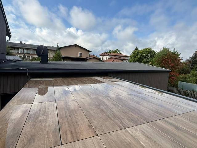 Große geflieste Dachterrasse mit Blick auf die umliegenden Häuser und grüne Umgebung.