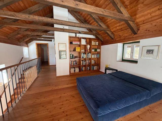 Helle Galerie mit Holzboden, Bücherregal und Schlafgelegenheit unter dem sichtbaren Dachstuhl.