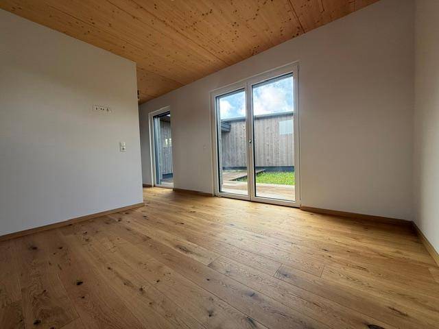 Heller Innenraum mit Holzboden, Holzdecke und großen Glasschiebetüren zum Außenbereich.
