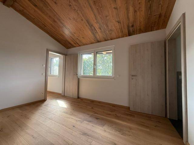 Schlafzimmer mit hellem Eichenparkett, Holzdecke und Fenstern mit Blick ins Grüne.