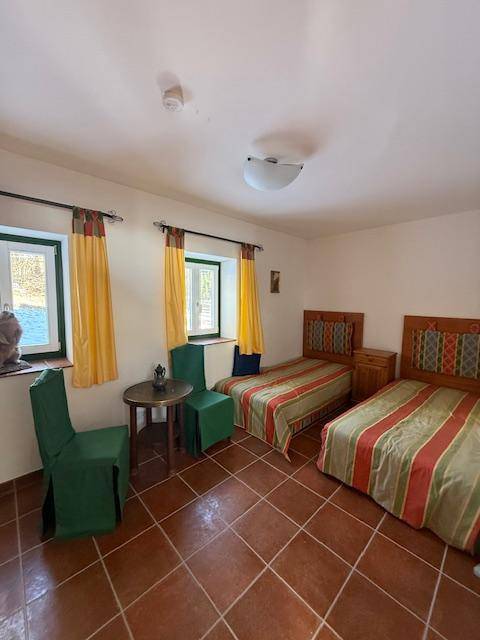Helles Schlafzimmer mit zwei Einzelbetten, Terrakottafliesen und farbigen Vorhängen.