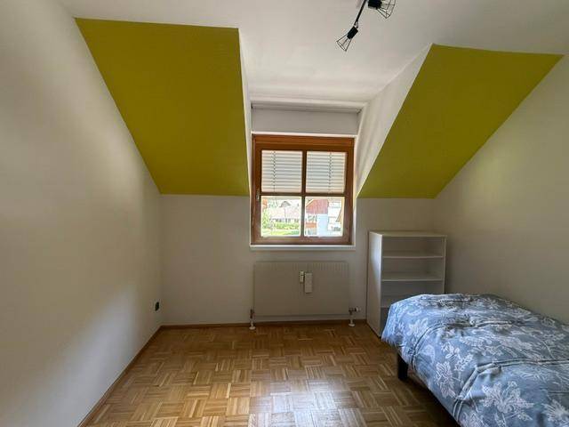 Schlafzimmer im Dachgeschoss mit Holzboden, Fenster und gelben Akzentflächen an den Wänden.