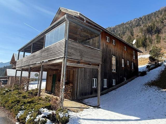 Traditionelles Holzhaus mit großem Balkon und Blick auf die verschneite Berglandschaft.