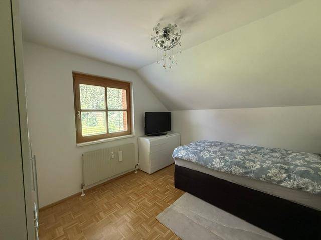 Helles Schlafzimmer mit Einzelbett, Holzboden und Fenster mit Blick ins Grüne.