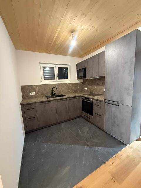 Moderne Küche mit grauen Fronten, dunklen Fliesen und Holzdecke, ausgestattet mit Geräten.
