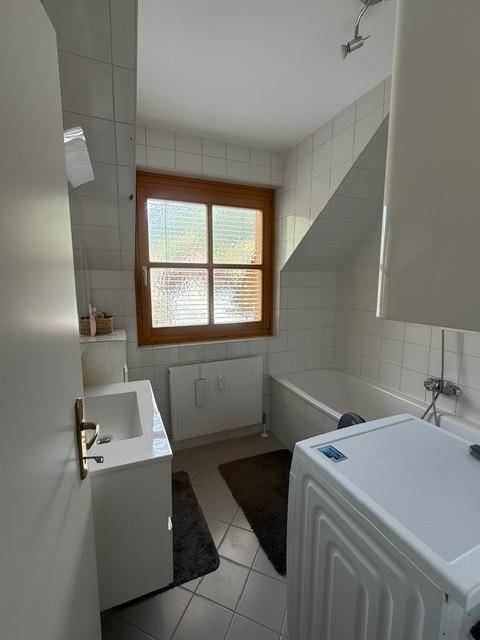 Badezimmer mit Badewanne, Waschbecken, Waschmaschine und Fenster im Dachgeschoss.