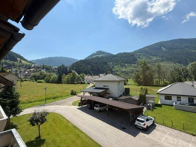 Weitläufiger Blick über die Landschaft mit Bergen, Häusern und Carports unter blauem Himmel.
