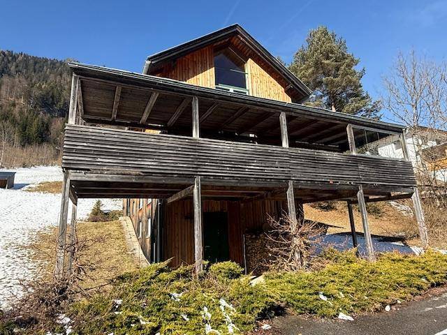 Charmantes Holzhaus mit überdachtem Balkon und Blick auf die umliegenden Berge.