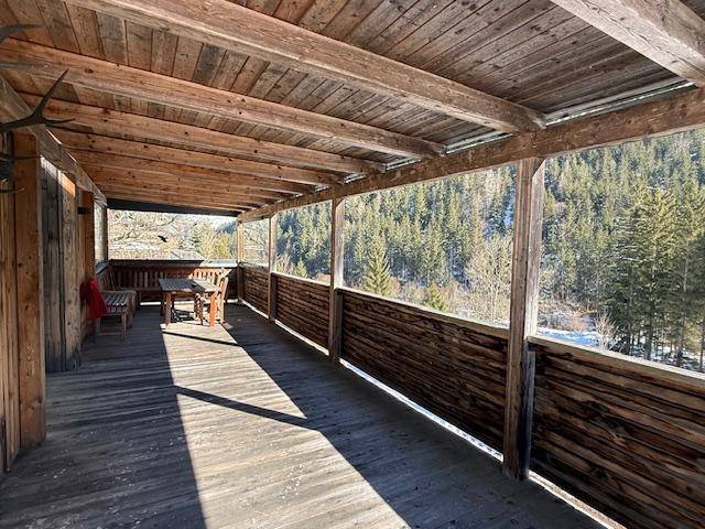 Geräumiger überdachter Holzbalkon mit Esstisch und weitem Blick auf den Wald.