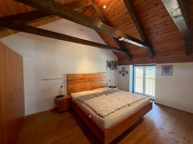 Schlafzimmer mit Holzbett, Dachschrägen und Zugang zu einem kleinen Balkon.