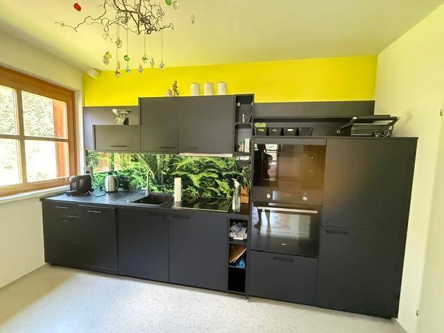 Moderne schwarze Einbauküche mit grüner Rückwand und gelber Akzentwand im Dachgeschoss.