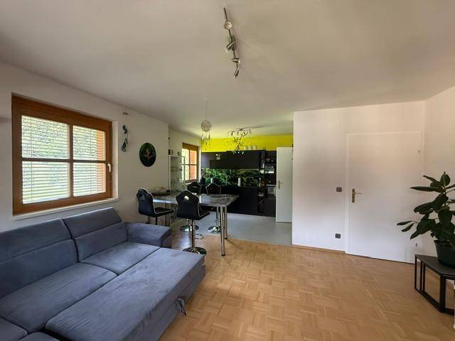 Offener Wohnbereich mit Sofa, Holzboden und Blick auf die moderne Küche mit gelber Wand.